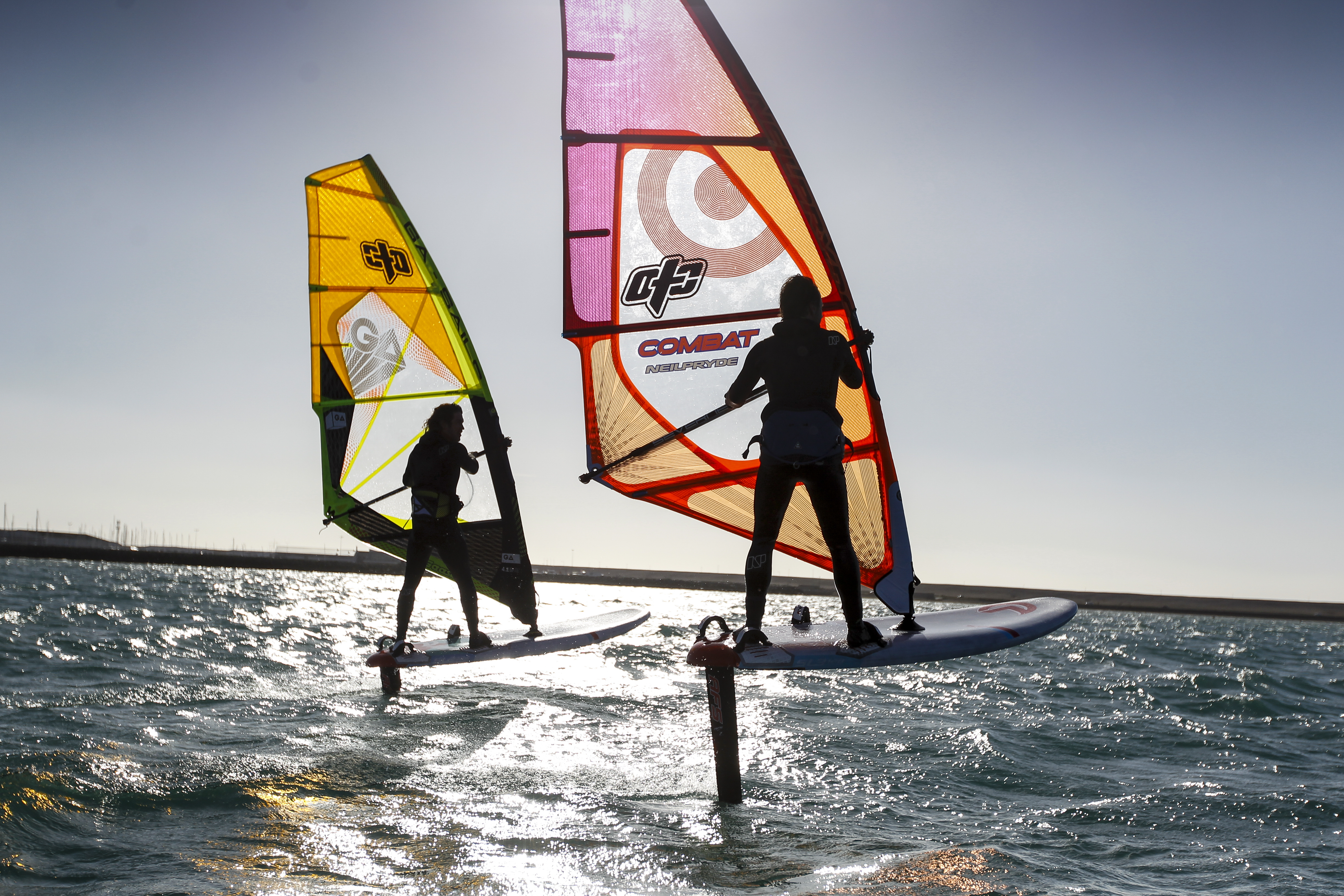 a silhouette of two foiling windsurfers against the sun and sea